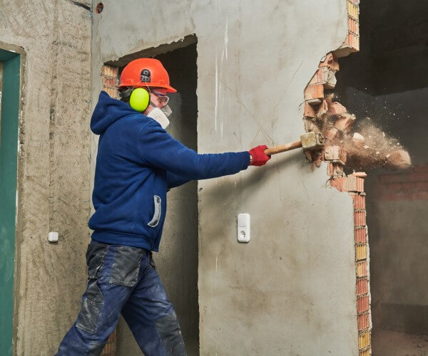 Laborer demolishing brick wall with sledgehammer
